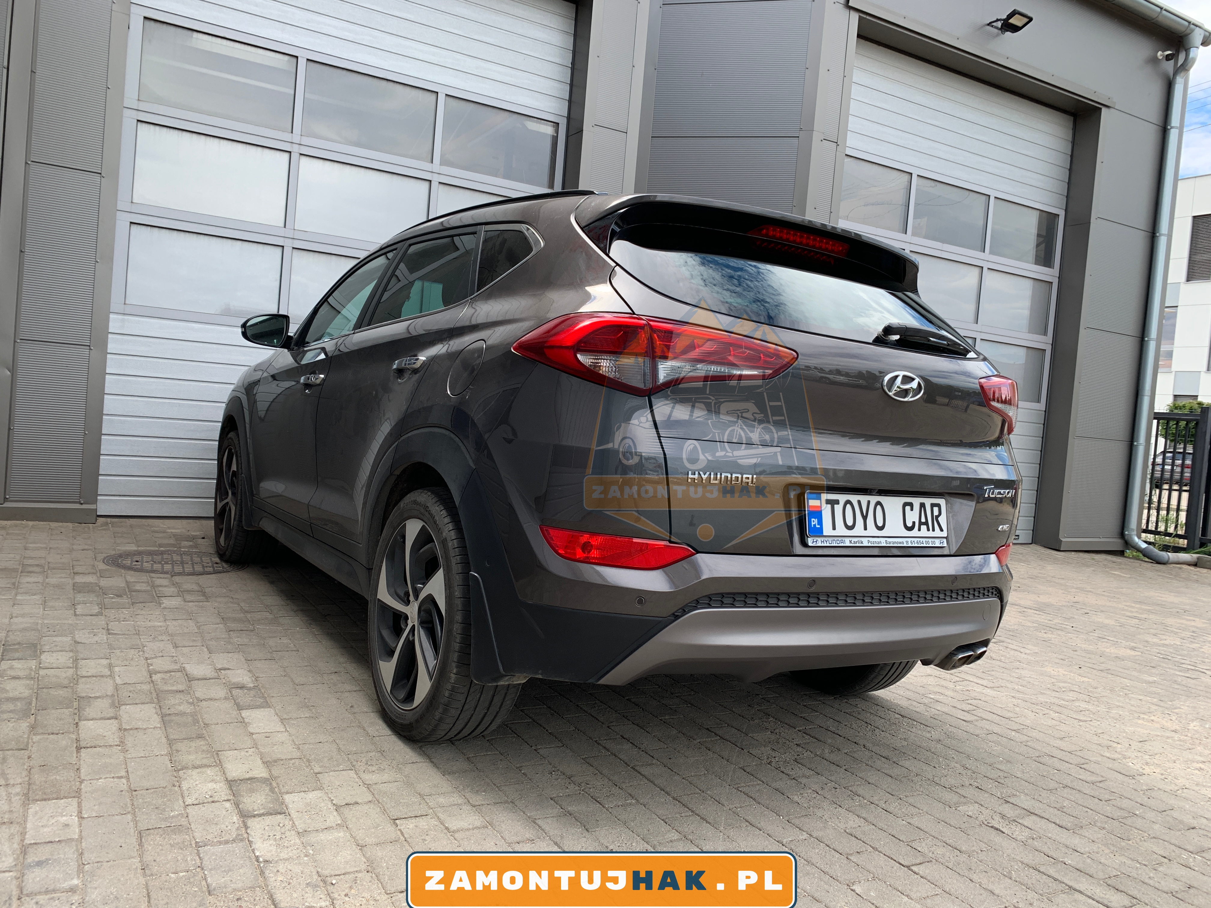 Zdjęcie Hyundaia Tucsona z zamontowanym hakiem holowniczym westfalia A40V, zdjęcie zostało zrobione, przy wypiętej kuli haka, z tyłu z lewej strony samochodu na tle serwisu zamontujhak.pl.